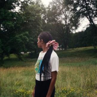 Gabrielle stands in a field looking over their shoulder and away from the camera.