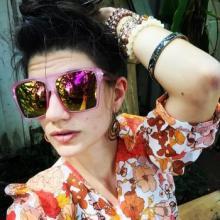 Kimberly in sunglasses and a shirt with orange flowers. Her brown hair is up & she is wearing bracelets.