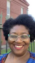 Image of of Black woman with rainbow-brim glasses, lipstick and a smile