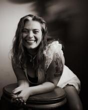 Kristen E Nelson's photo by Julius Schlosburg. Black and white image of Kristen sitting and smiling.