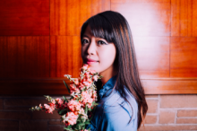Chinese American poet Jane Wong with long black and brown hair, holding flowers in a blue shirt