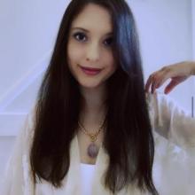 Kailey Tedesco is a white woman with long dark hair. She is wearing a white shawl & a large amethyst necklace.