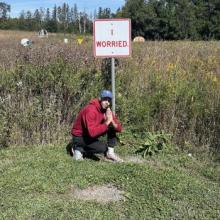 The author genuflects below a sign that reads "I Worried" 
