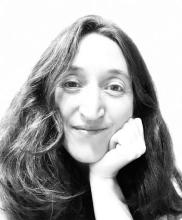 black and white photo of the poet resting chin/jaw on hand, closed mouth smile, hair in the light past the frame