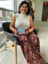 Nuha has brown skin, short black hair, and wears glasses, a white tank top, and colorful pants.