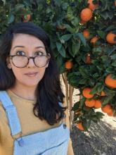 Latina with long hair and glasses standing next to an orange tree