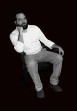 Bearded man sitting down with his hand on his chin