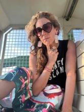 The photo is me with black heart shaped sunglasses, a black T-shirt a colorful skirt, and my hair is in a braid to the side