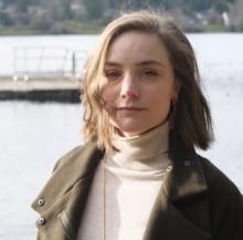 close up portrait of white femme with short brown hair, green coat, and a lake in the background