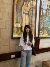 A woman with brown hair, a white shirt, and light blue jeans smiling at the camera.
