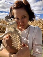 A woman with short dark hair embraces a plastic dog skeleton. In the background, a perfect Ohio sky.