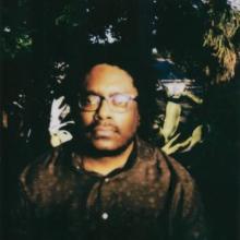 Poet Randall Tyrone outside, surrounded by plants and brick walls