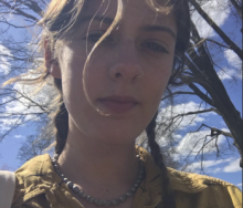 Picture of Scout in a yellow shirt with hair in braids against the sky and a tree. 