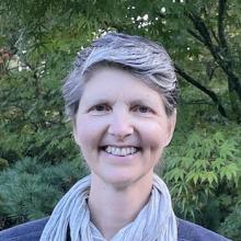 Front-facing portrait of author with short graying hair, with leafy trees in background