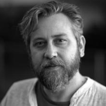 In this black and white photo, Christopher Shipman stares at the camera, slightly amused.