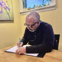 A photo of the poet Michael Kleber-Diggs, a Black man with gray hair wearing a black sweater while writing in a notebook.