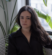 Long-haired woman seating in a wired chair indoors with a house palm tree behind